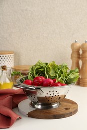 Photo of Wet radish in colander on white table. Space for text