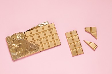 Shiny golden chocolate bar with foil on pink background, flat lay