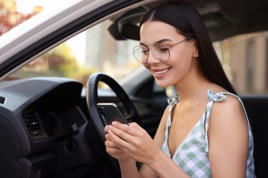 Happy young woman with smartphone sitting in car