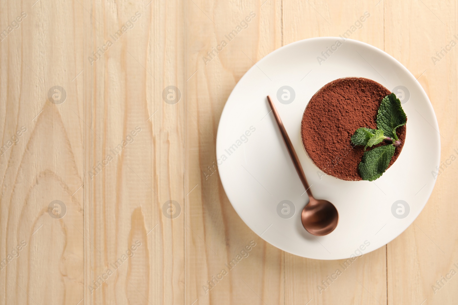 Photo of Tasty tiramisu and mint in glass on light wooden table, top view. Space for text