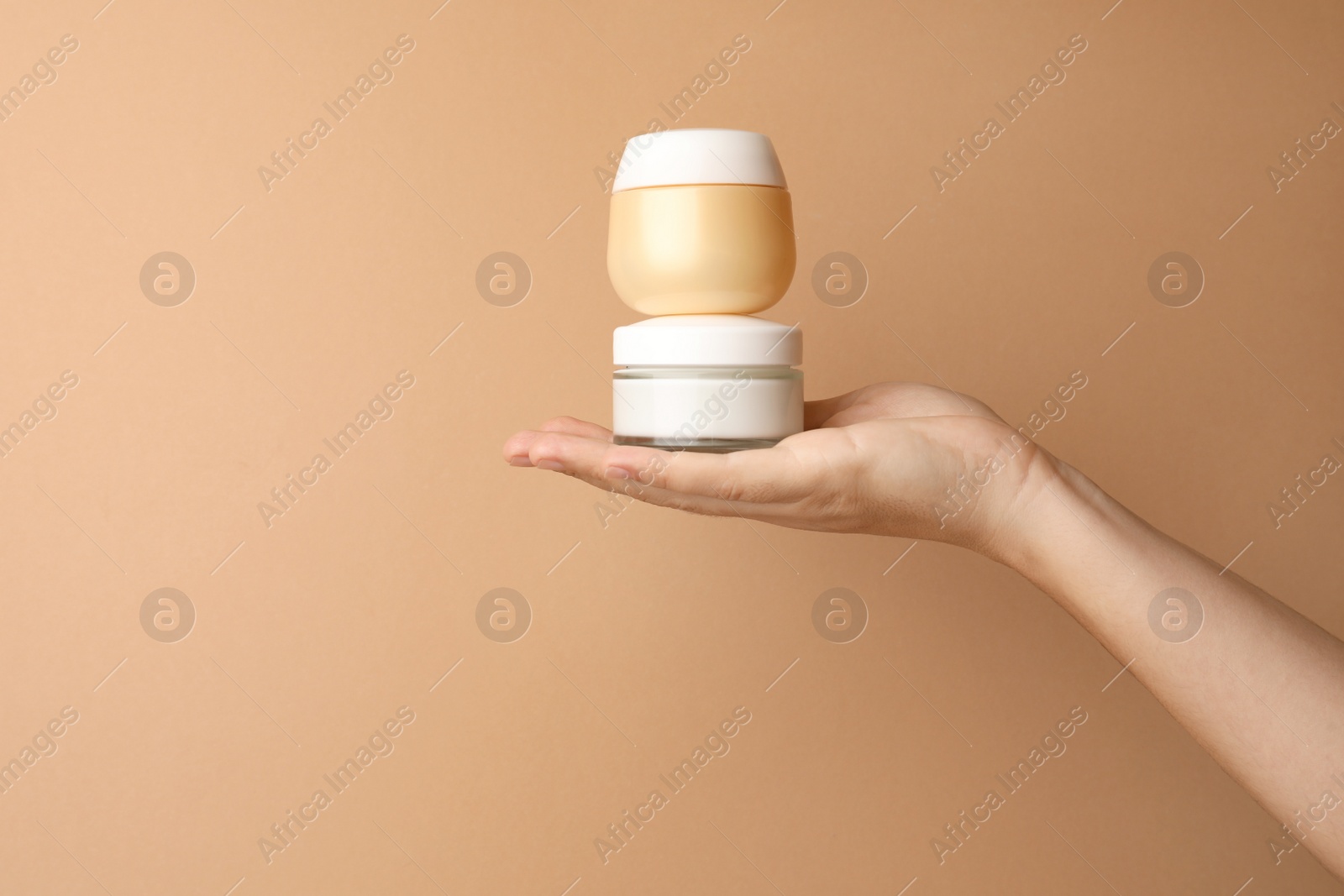 Photo of Woman holding jars of face cream on beige background, closeup. Space for text