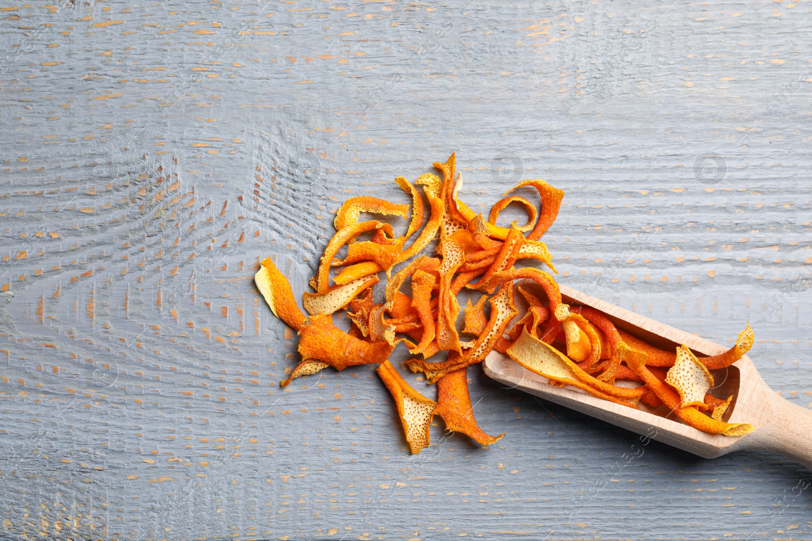 Photo of Scoop with dry orange peels on wooden table, flat lay. Space for text