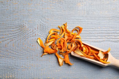 Photo of Scoop with dry orange peels on wooden table, flat lay. Space for text
