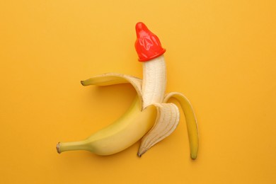 Photo of Banana with condom on orange background, top view. Safe sex concept