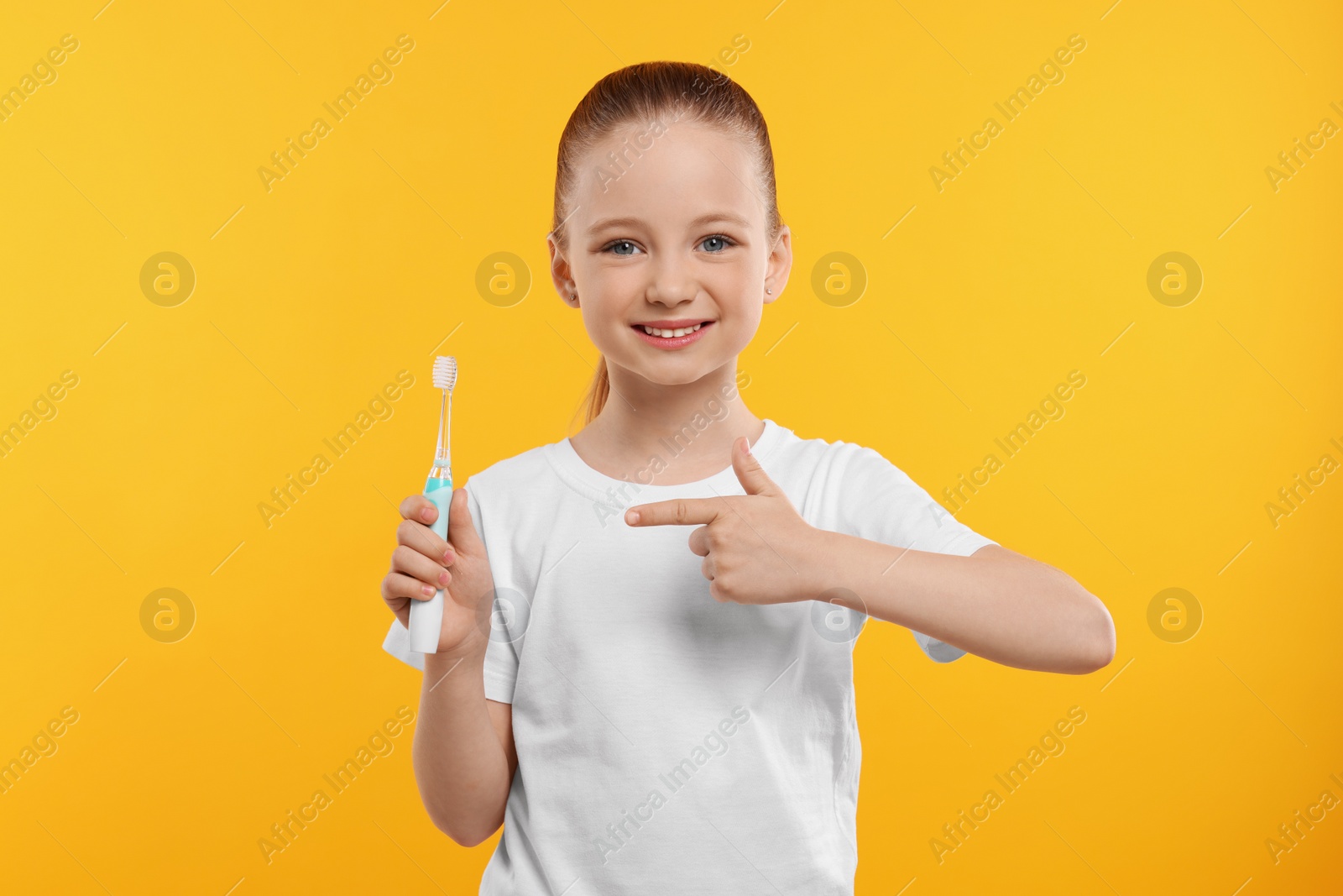 Photo of Happy girl holding electric toothbrush on yellow background