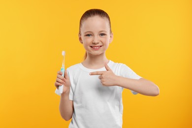 Happy girl holding electric toothbrush on yellow background