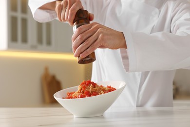 Photo of Professional chef adding pepper into delicious dish at white marble table indoors, closeup