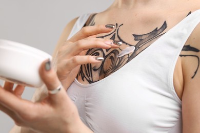 Woman applying healing cream onto her tattoos against grey background, closeup