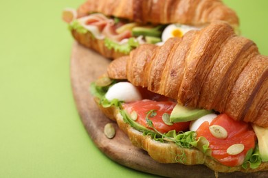 Photo of Delicious croissants with avocado and salmon on green table, closeup. Space for text