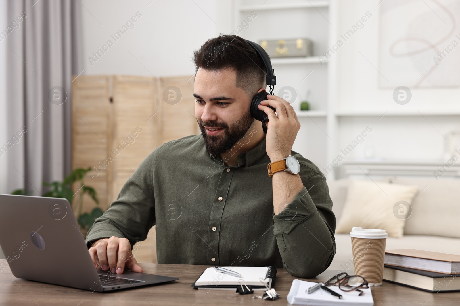 Photo of E-learning. Young man using laptop during online lesson at wooden table indoors