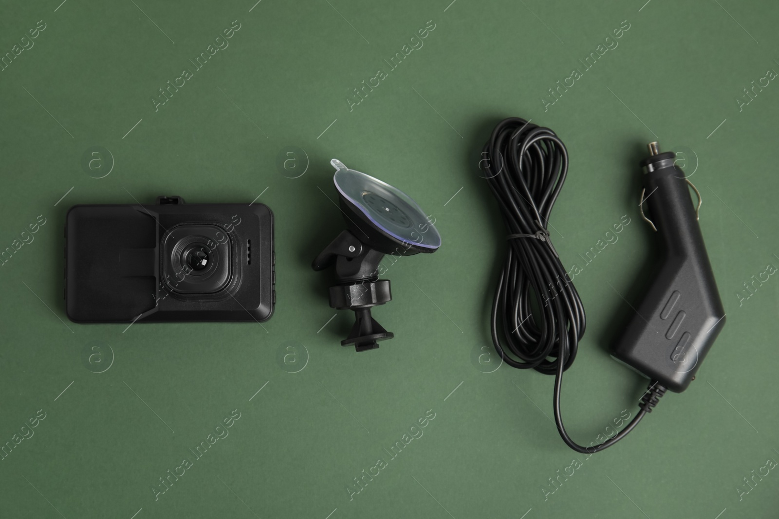 Photo of Modern car dashboard camera, suction mount and charger on dark green background, flat lay