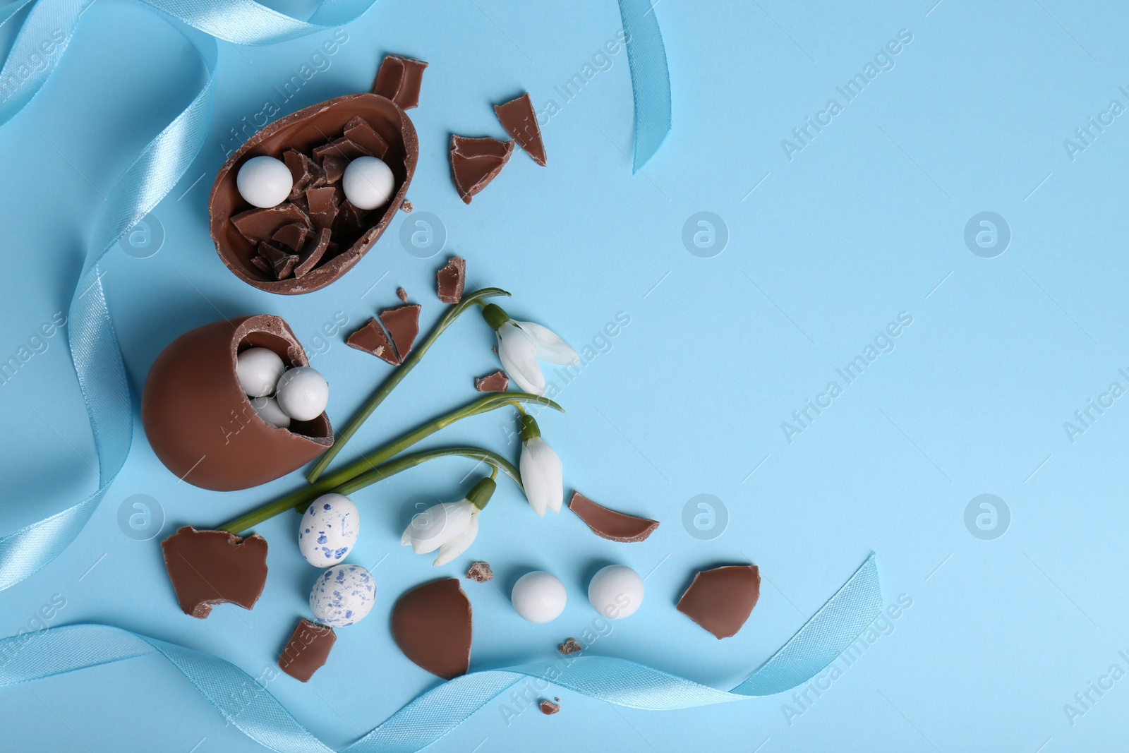 Photo of Flat lay composition with tasty broken chocolate eggs and beautiful decor on light blue background. Space for text