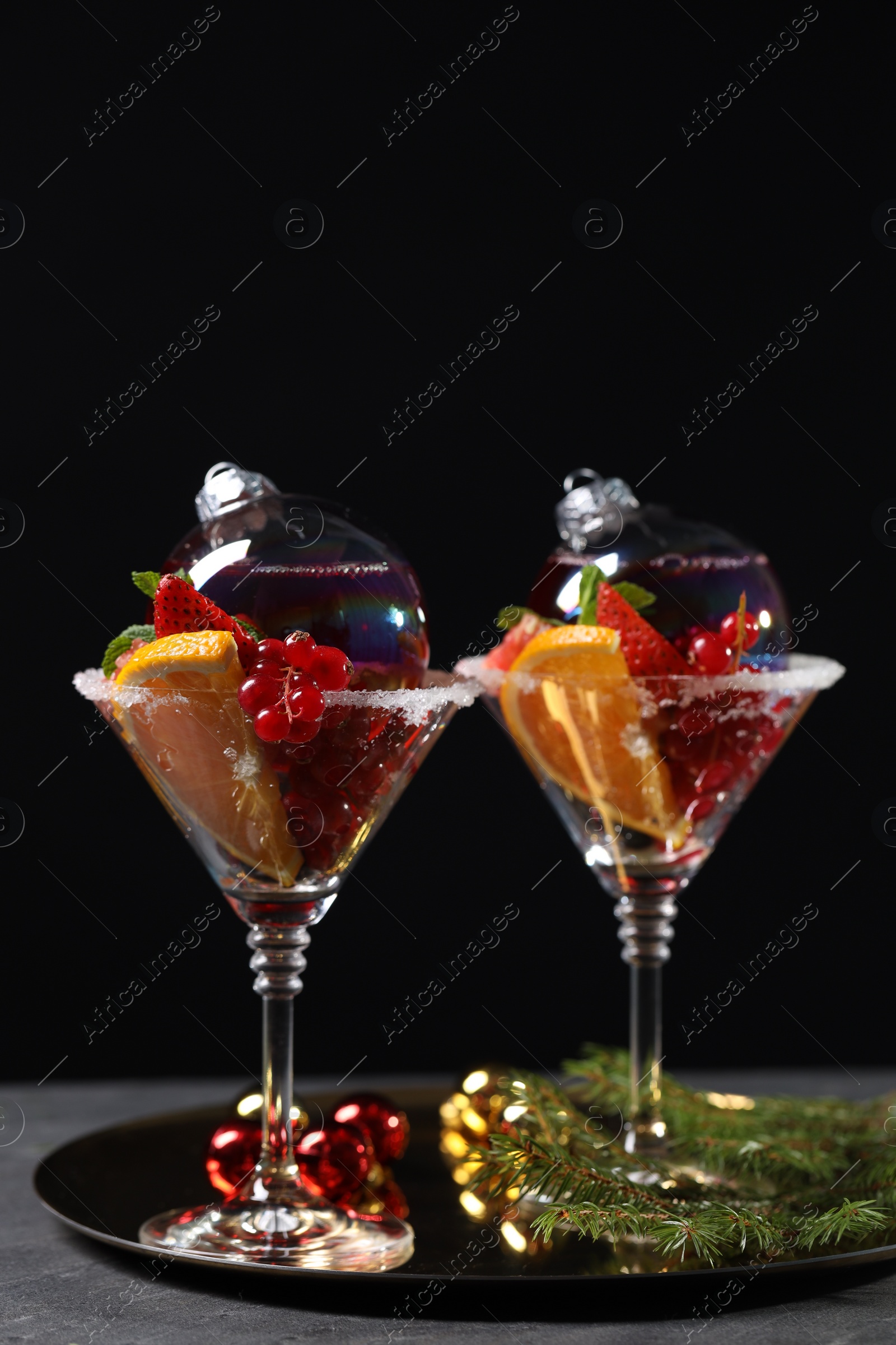 Photo of Creative presentation of Christmas Sangria cocktail in baubles and glasses on grey table against black background