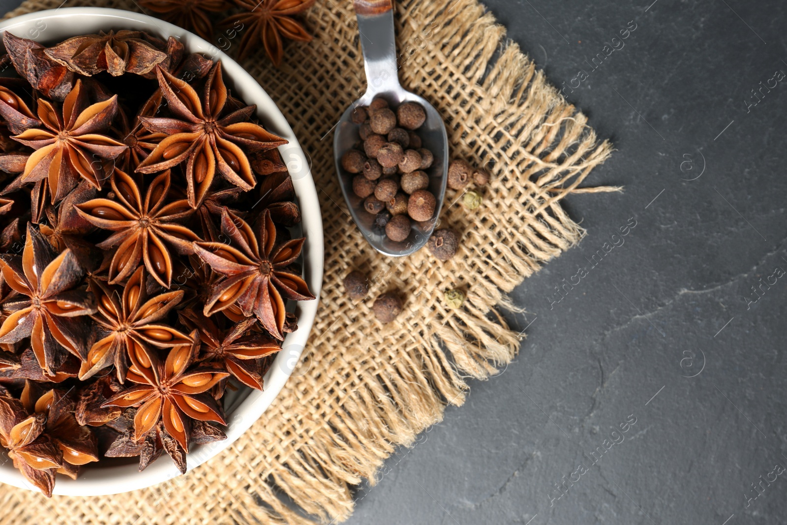 Photo of Bowl with aromatic anise stars and pepper on dark table, flat lay. Space for text