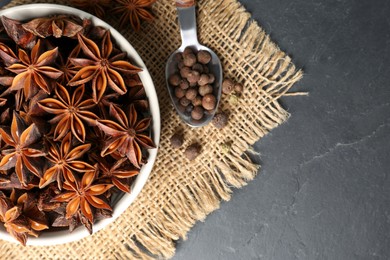 Bowl with aromatic anise stars and pepper on dark table, flat lay. Space for text