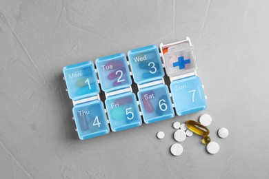 Weekly pill box with medicaments on grey table, flat lay