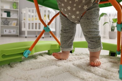 Photo of Little baby making first steps with toy walker on carpet at home, closeup