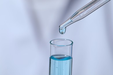 Photo of Dripping liquid from pipette into test tube on blurred background, closeup