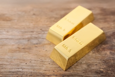 Photo of Shiny gold bars on wooden table. Space for text