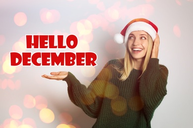 Image of Hello December greeting card. Happy woman in Santa hat on white background, bokeh effect