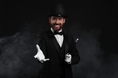 Happy magician holding wand in smoke on black background