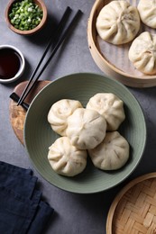 Photo of Delicious bao buns (baozi), chopsticks, soy sauce and green onion on grey table, flat lay