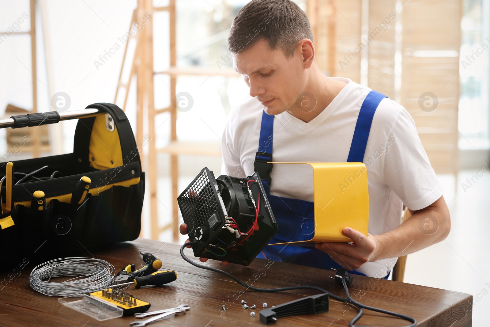 Photo of Professional technician repairing electric fan heater at table indoors