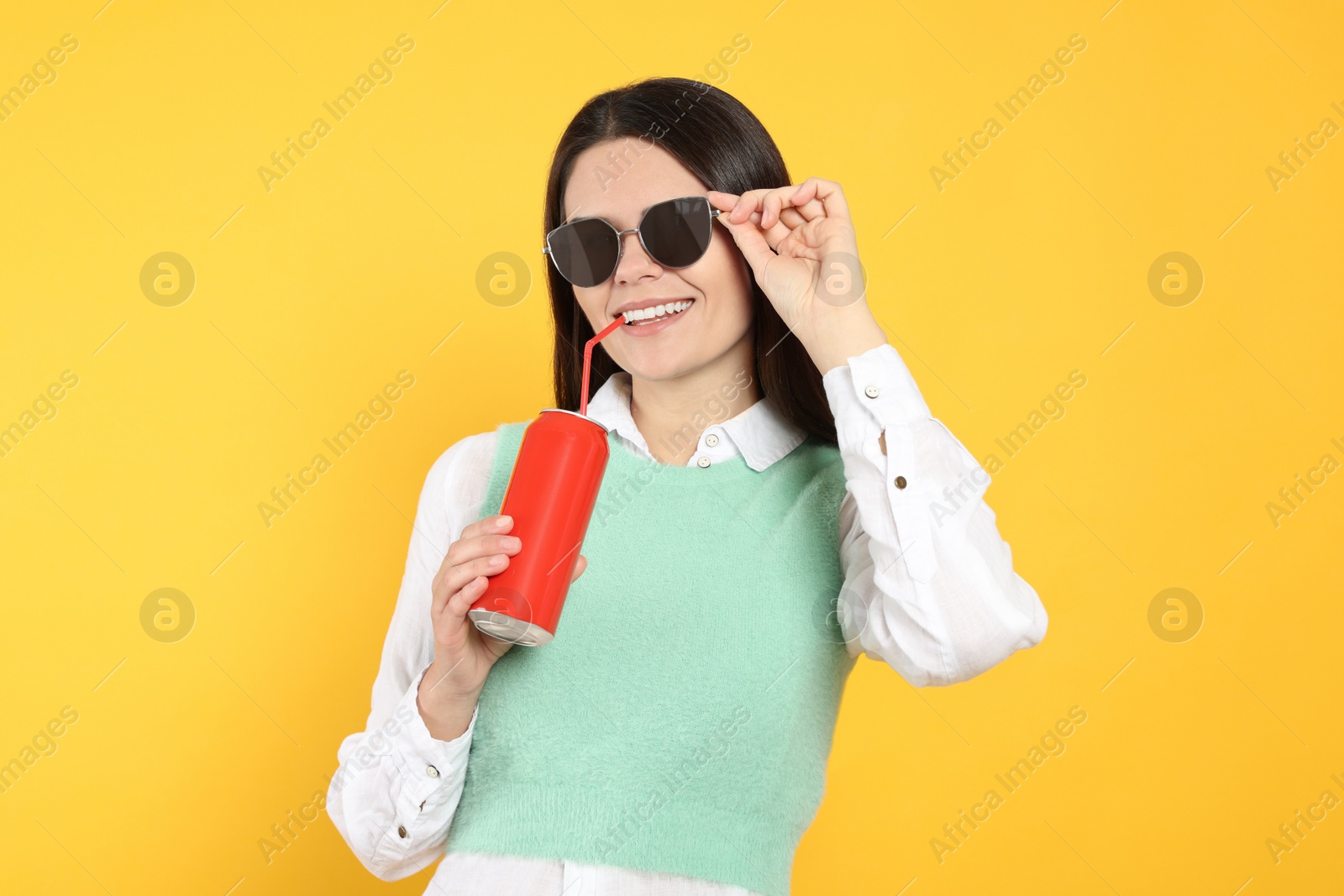 Photo of Beautiful happy woman drinking from red beverage can on yellow background