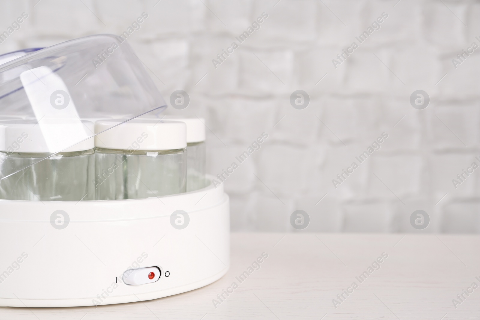 Photo of Modern yogurt maker with empty jars on white wooden table, closeup. Space for text