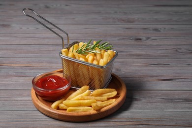 Photo of Tasty French fries, rosemary and ketchup on grey wooden table. Space for text