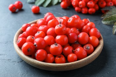 Photo of Wooden plate with fresh ripe rowan berries on black table, closeup
