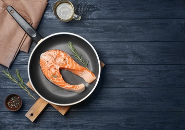 Photo of Frying pan with fresh raw salmon steak on wooden background, top view