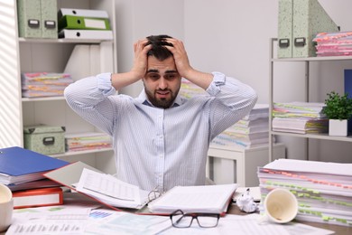 Photo of Overwhelmed man surrounded by documents at workplace in office