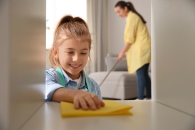 Photo of Little girl helping her mother with cleaning living room