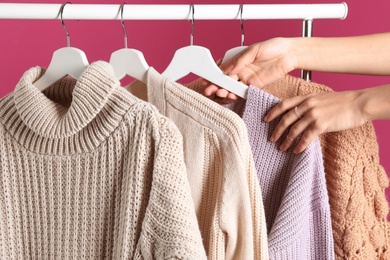 Photo of Woman choosing sweater on rack against color background, closeup