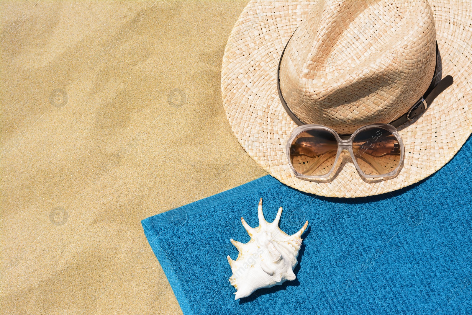 Photo of Soft blue beach towel, sunglasses, straw hat and seashell on sand, flat lay. Space for text