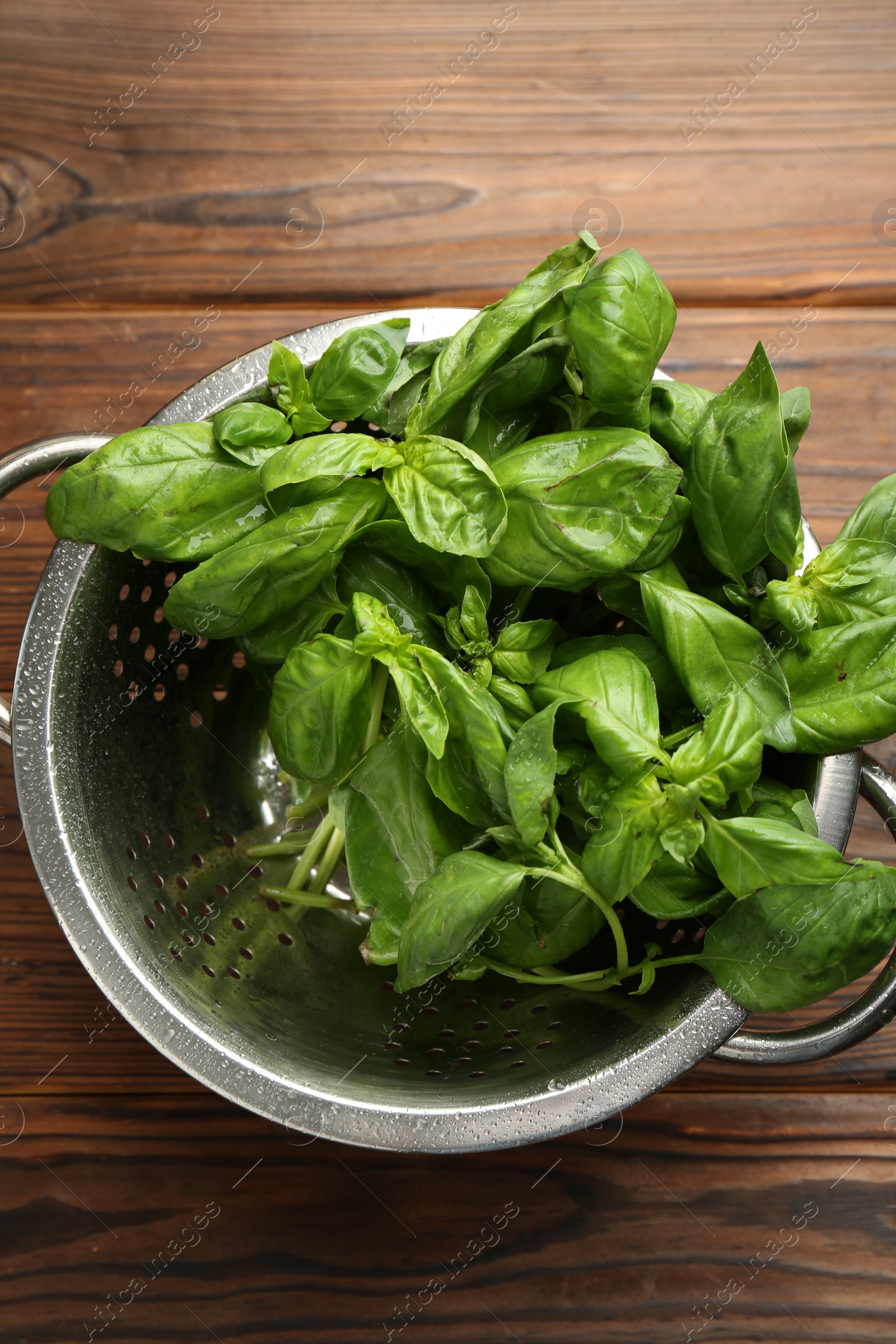 Photo of Metal colander with fresh basil leaves on wooden table, top view