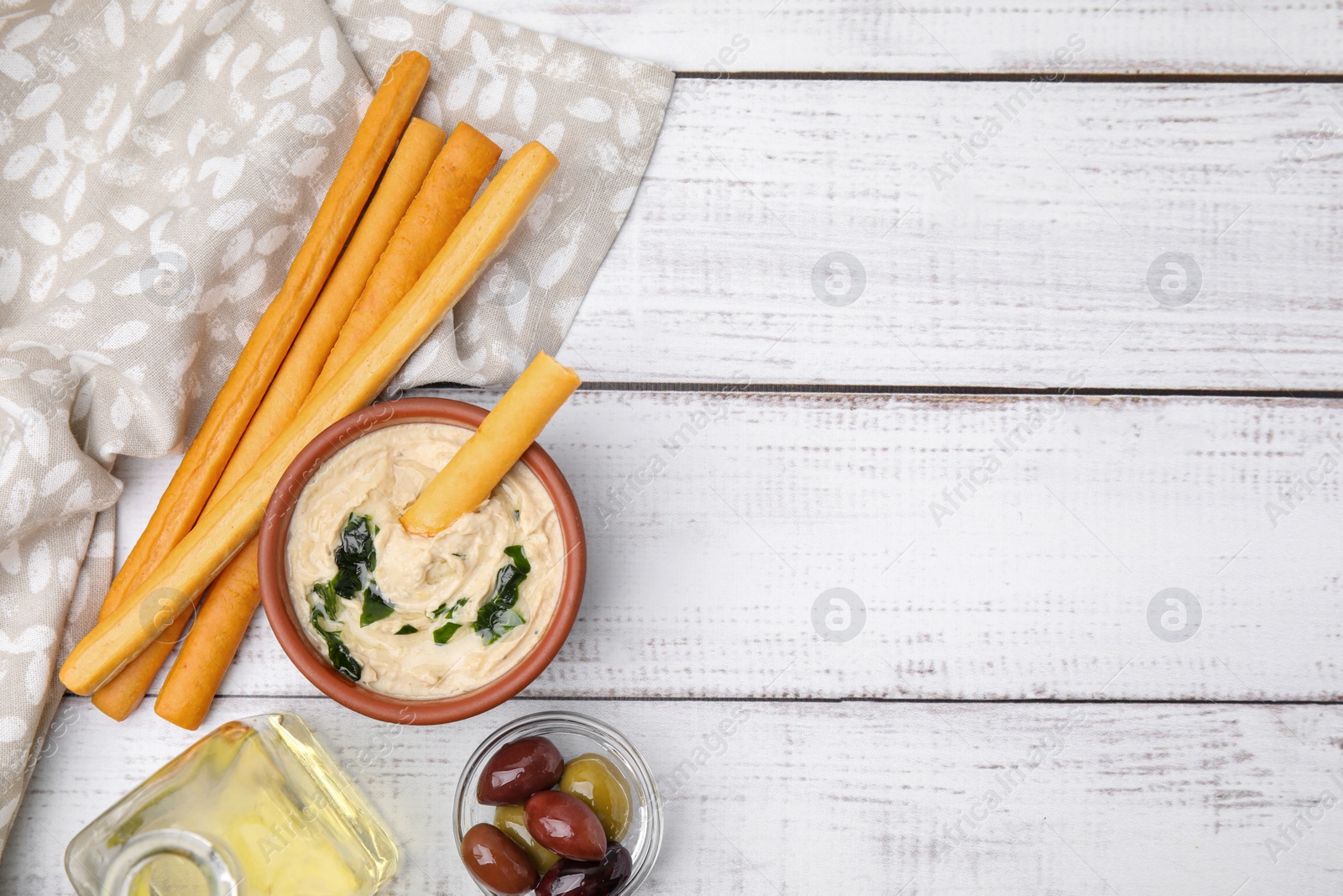 Photo of Delicious hummus with grissini sticks and olives on white wooden table, flat lay. Space for text
