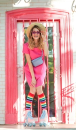 Photo of Happy girl with retro roller skates standing near pink door