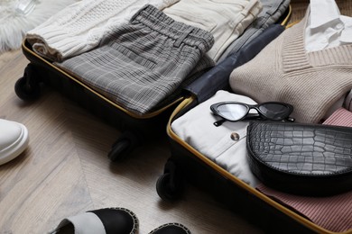 Photo of Open suitcase with folded clothes and accessories on floor, closeup