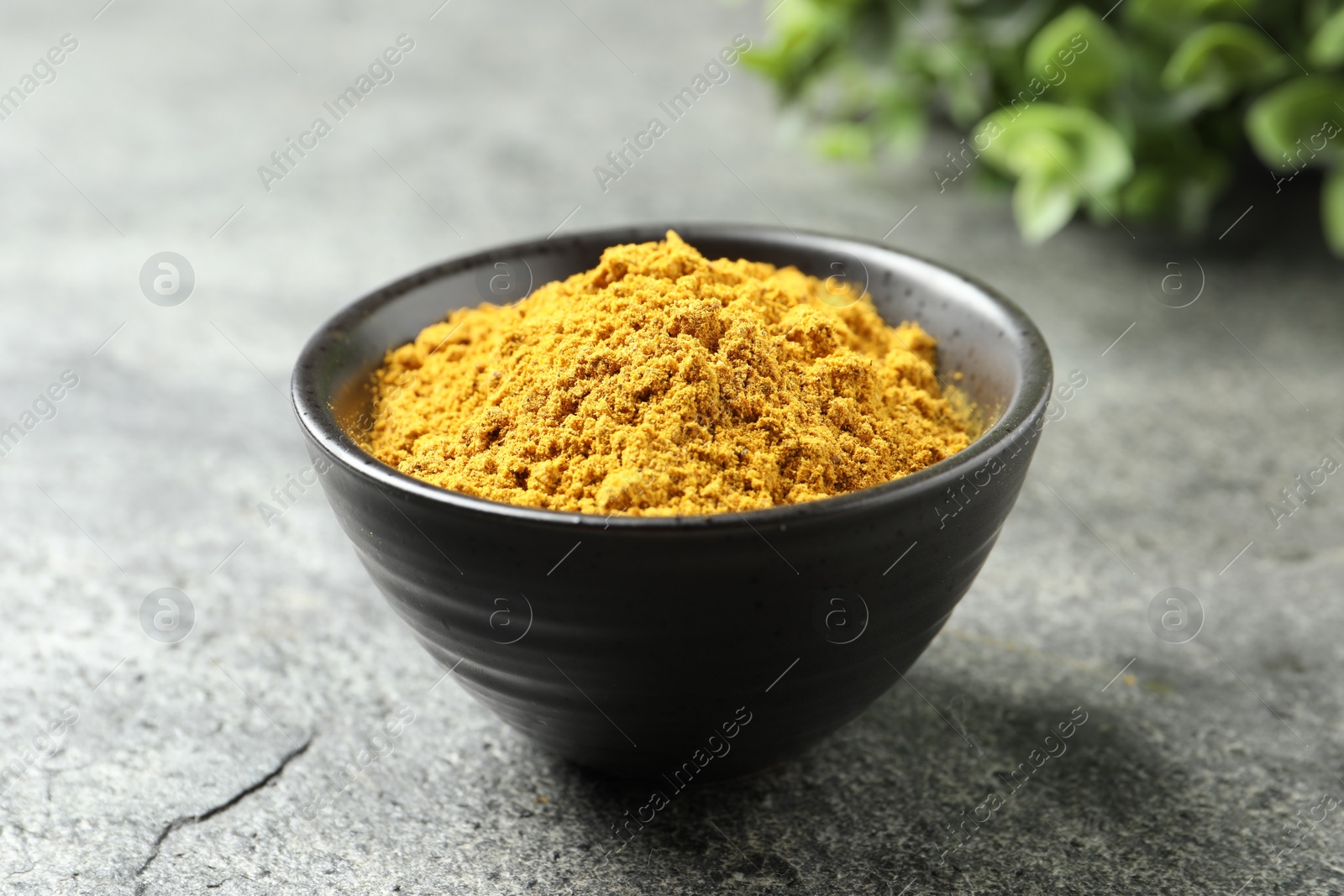 Photo of Dry curry powder in bowl on dark textured table, closeup