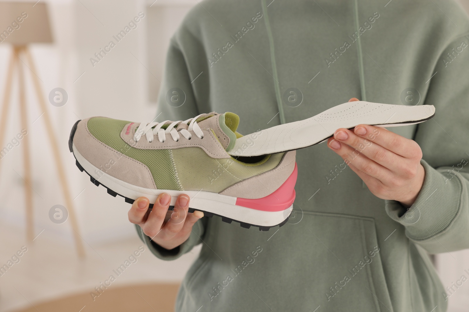 Photo of Woman putting orthopedic insole into shoe indoors, closeup. Foot care