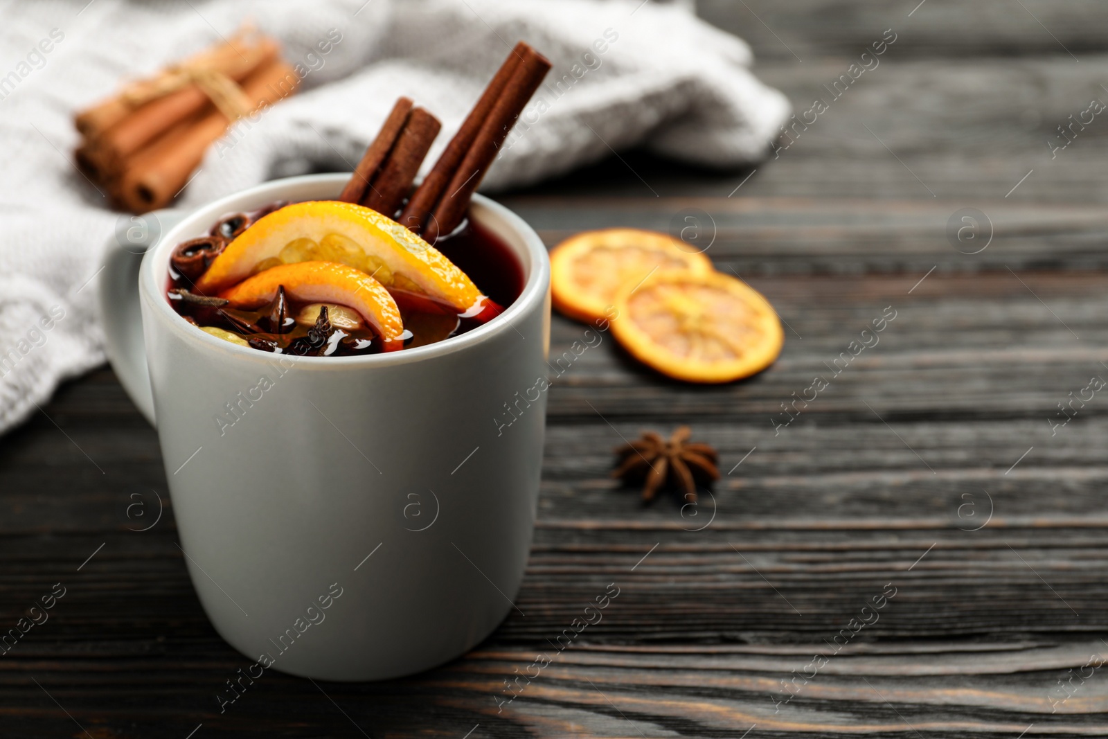 Photo of Cup of tasty mulled wine on black wooden table. Space for text