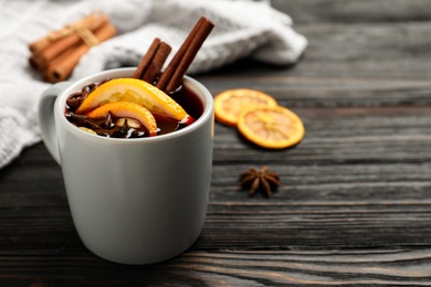 Photo of Cup of tasty mulled wine on black wooden table. Space for text