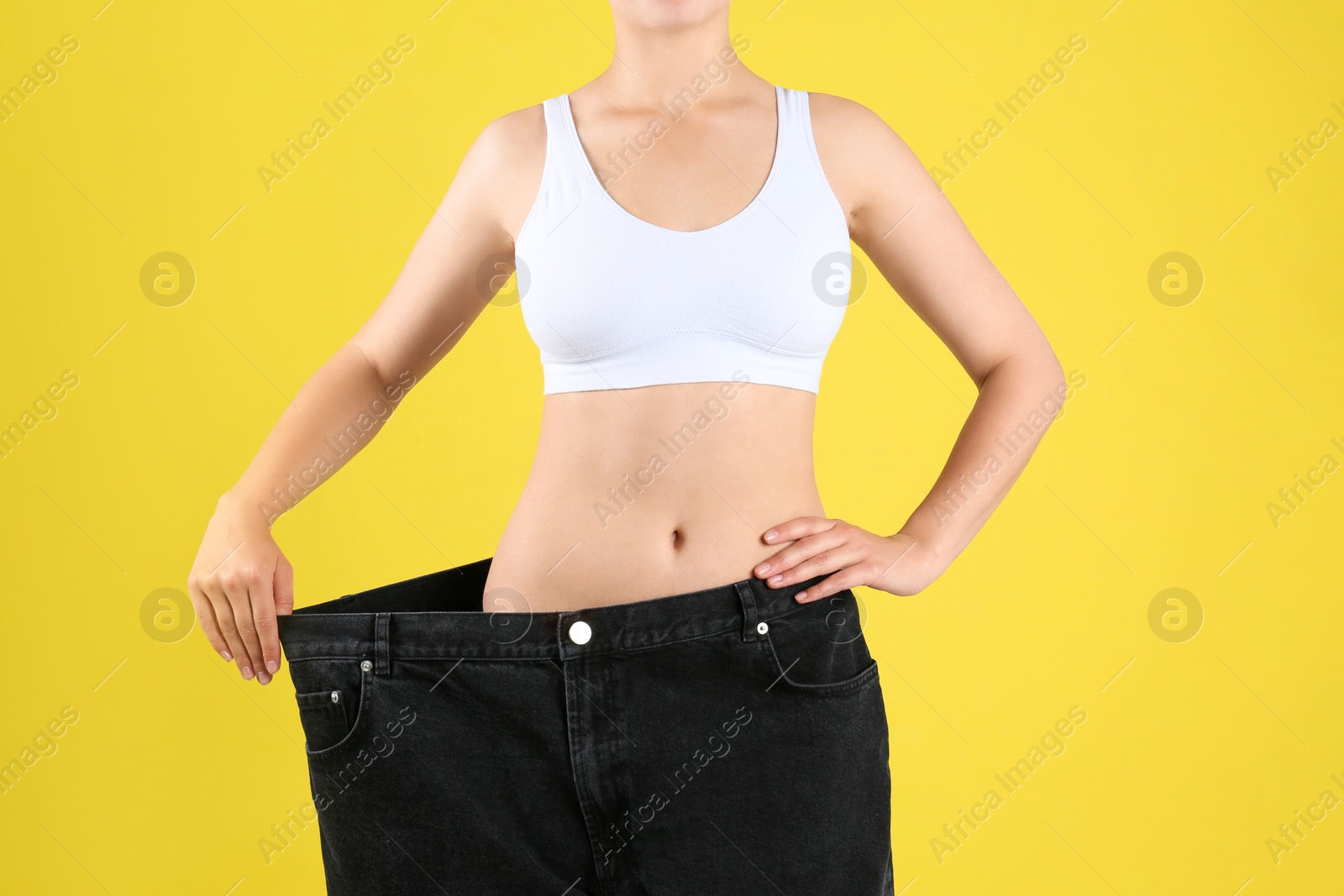 Photo of Young slim woman wearing oversized jeans on yellow background, closeup