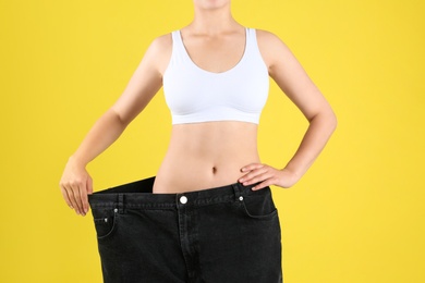 Photo of Young slim woman wearing oversized jeans on yellow background, closeup