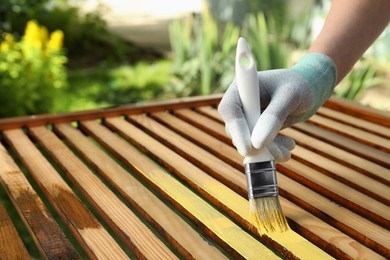 Woman painting wooden surface with yellow dye outdoors, closeup. Space for text