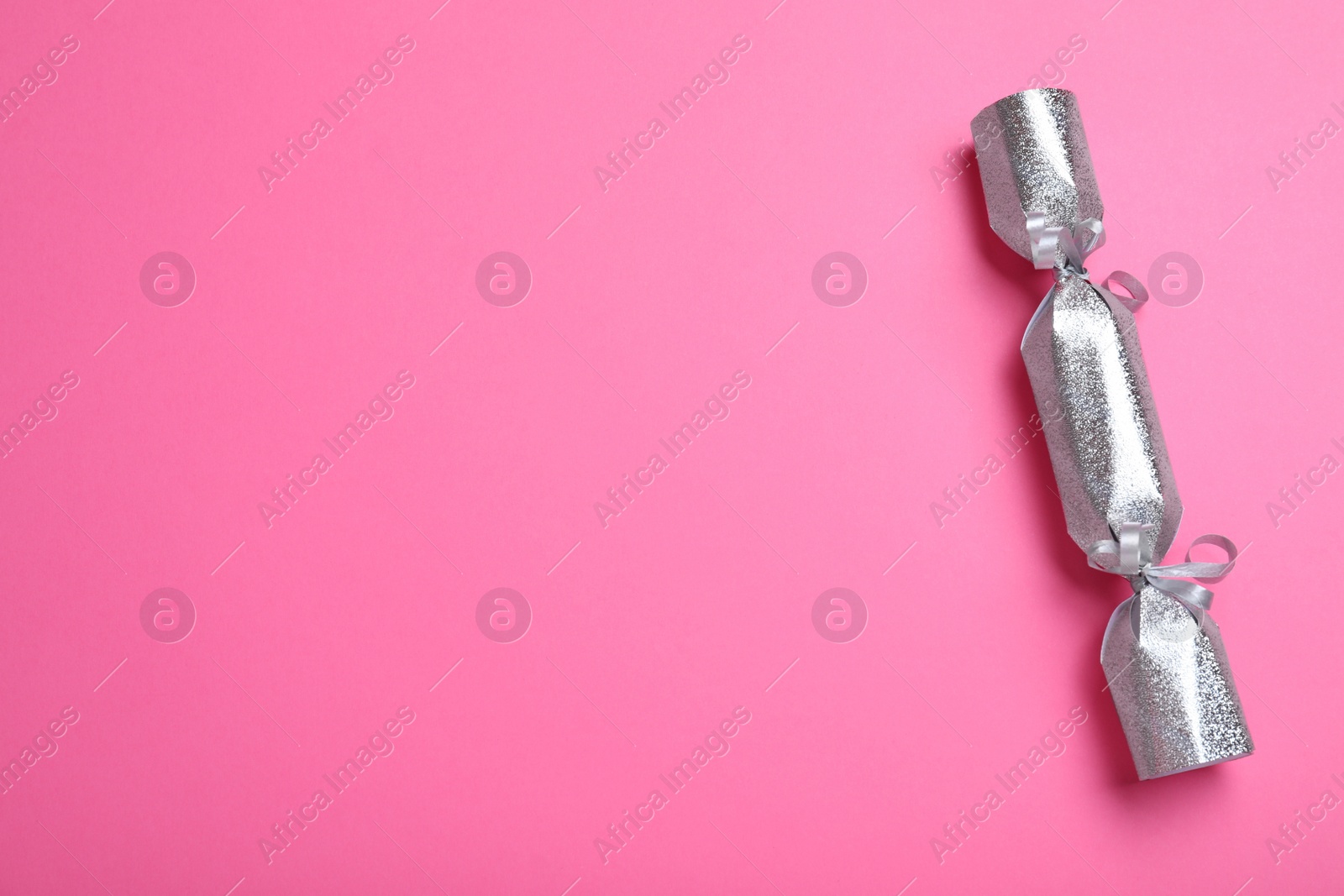 Photo of Silver Christmas cracker on pink background, top view. Space for text