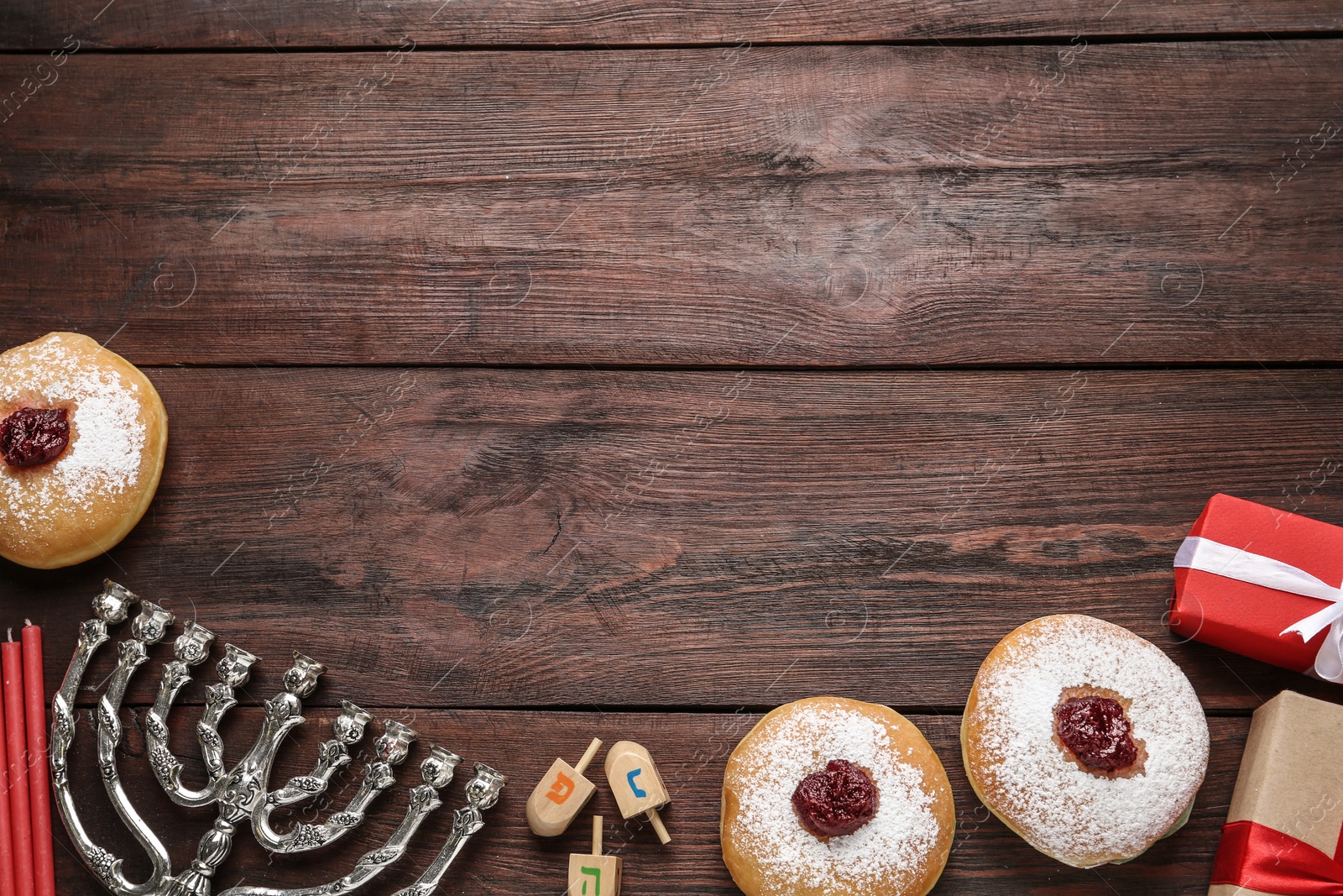 Photo of Hanukkah traditional menorah, candles, doughnuts, dreidels with letters He, Pe, Nun, Gimel on wooden background, flat lay. Space for text