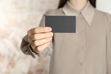Photo of Woman holding blank business card on blurred background, closeup. Mockup for design